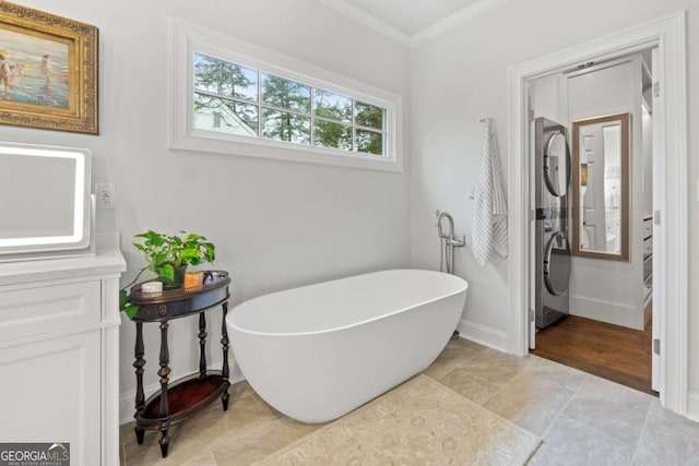 bathroom with tile patterned floors, stacked washing maching and dryer, a tub, and ornamental molding