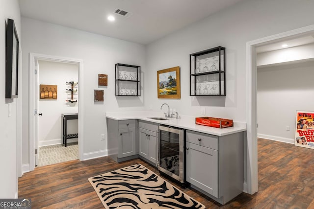 bar featuring beverage cooler, visible vents, dark wood-style flooring, a sink, and indoor wet bar