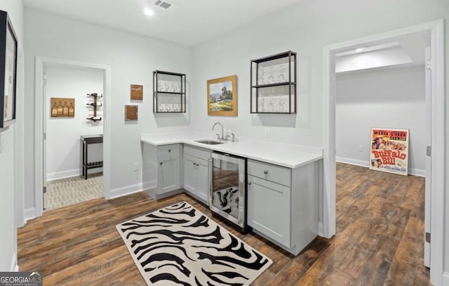 bar featuring gray cabinetry, sink, wine cooler, and dark wood-type flooring