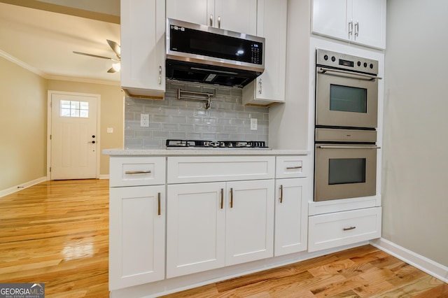 kitchen featuring backsplash, light wood-type flooring, ornamental molding, white cabinetry, and stainless steel appliances