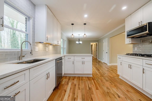 kitchen featuring light wood-type flooring, stainless steel appliances, sink, white cabinets, and hanging light fixtures