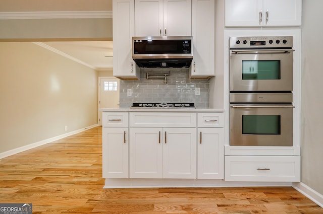 kitchen featuring backsplash, appliances with stainless steel finishes, light hardwood / wood-style floors, white cabinets, and ornamental molding