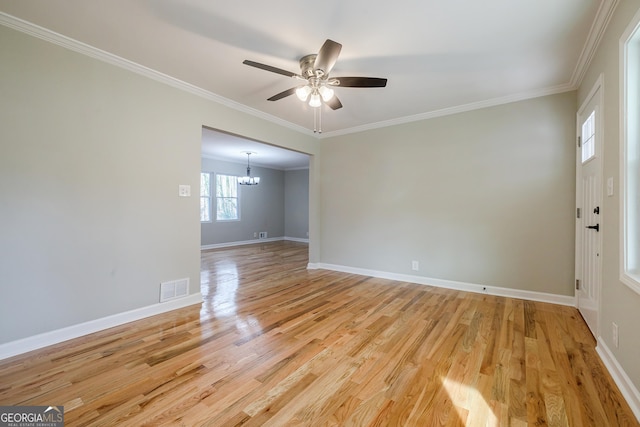 empty room featuring ceiling fan with notable chandelier, light wood-type flooring, and crown molding