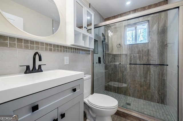 bathroom featuring tasteful backsplash, vanity, a shower with shower door, and toilet