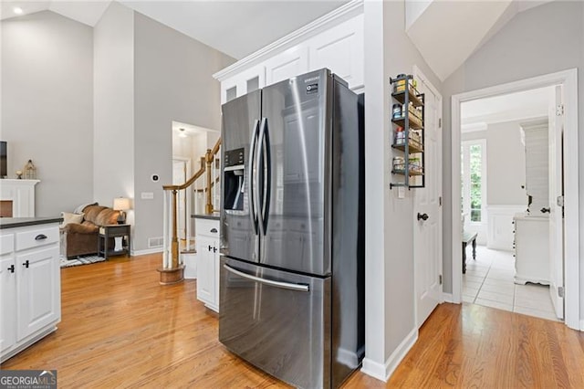 kitchen featuring vaulted ceiling, dark countertops, stainless steel fridge, and white cabinetry