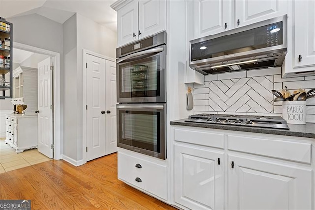 kitchen featuring stainless steel appliances, dark countertops, white cabinetry, and decorative backsplash