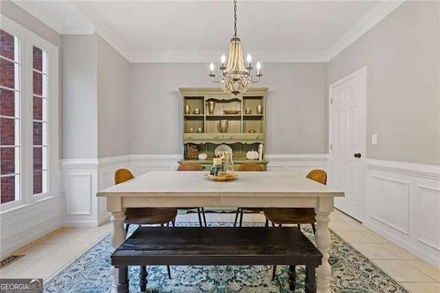 dining room with light tile patterned floors, ornamental molding, a wainscoted wall, and a notable chandelier