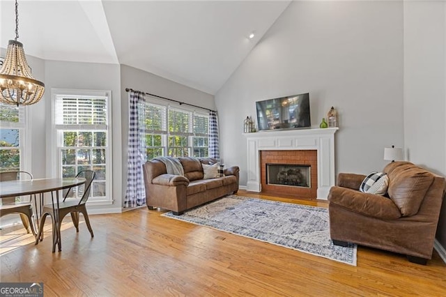 living area with high vaulted ceiling, a brick fireplace, a chandelier, and wood finished floors