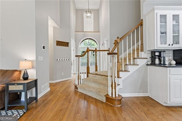 entryway featuring a towering ceiling, light wood finished floors, stairs, and baseboards