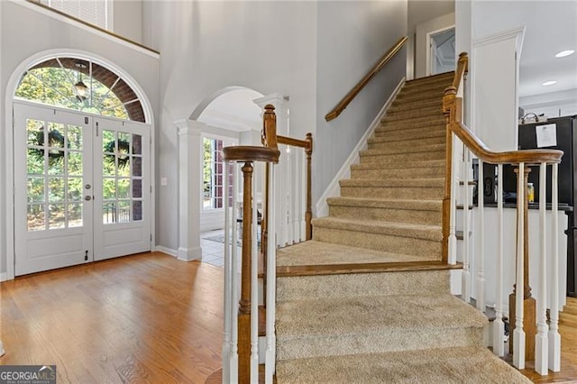 entrance foyer with stairway, a towering ceiling, light wood-style flooring, and ornate columns