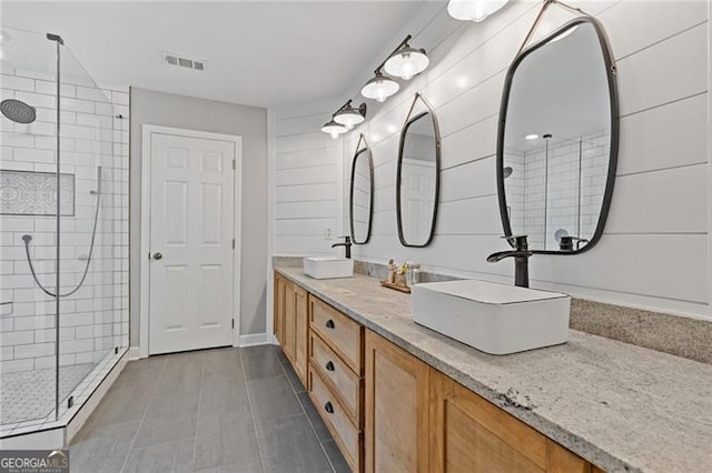 full bathroom with double vanity, tiled shower, a sink, and visible vents