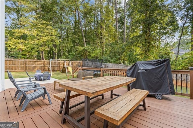 wooden deck with a fenced backyard, a trampoline, outdoor dining area, and area for grilling