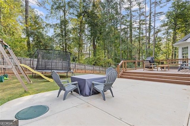 view of patio with a trampoline, a playground, a fenced backyard, and a deck