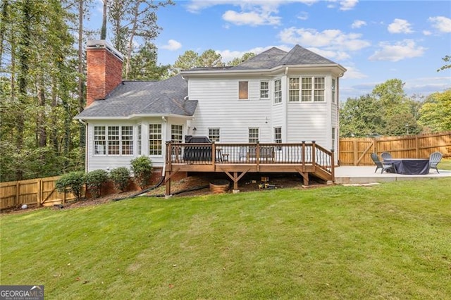 rear view of house featuring a deck, a yard, a chimney, and a fenced backyard