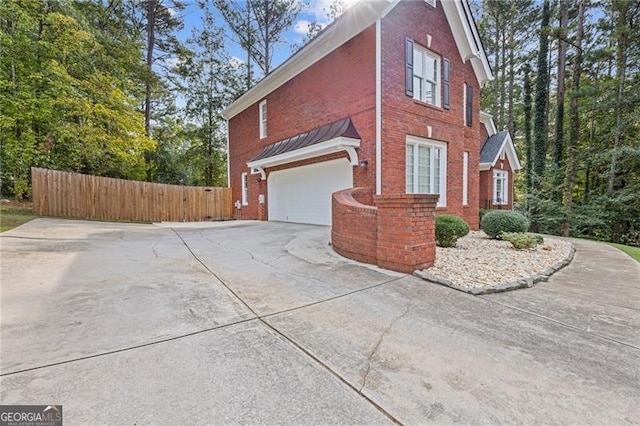 view of property exterior with a garage, driveway, brick siding, and fence