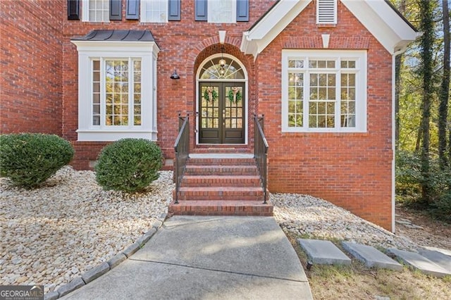 view of exterior entry with french doors, brick siding, and a standing seam roof