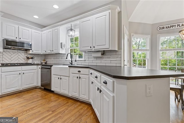 kitchen featuring stainless steel appliances, dark countertops, a peninsula, and white cabinetry