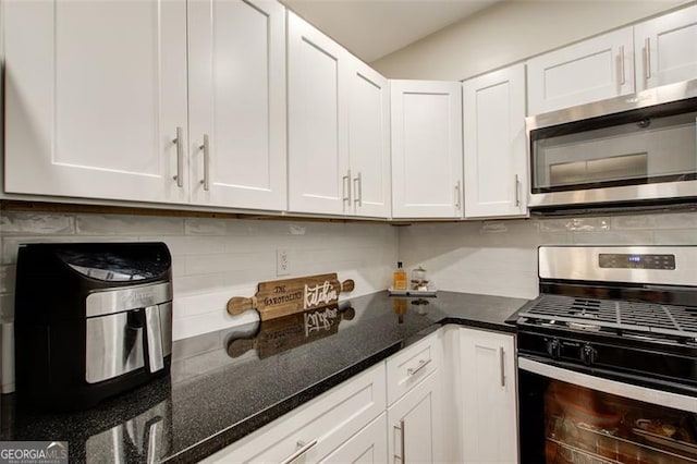 kitchen featuring white cabinets, appliances with stainless steel finishes, decorative backsplash, and dark stone counters