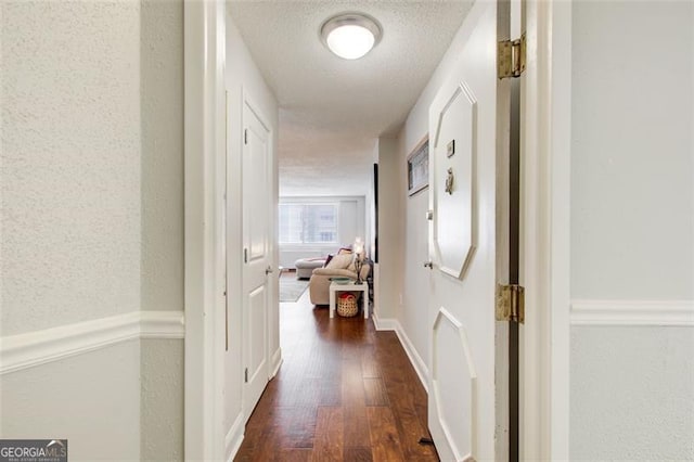 corridor with dark hardwood / wood-style flooring and a textured ceiling