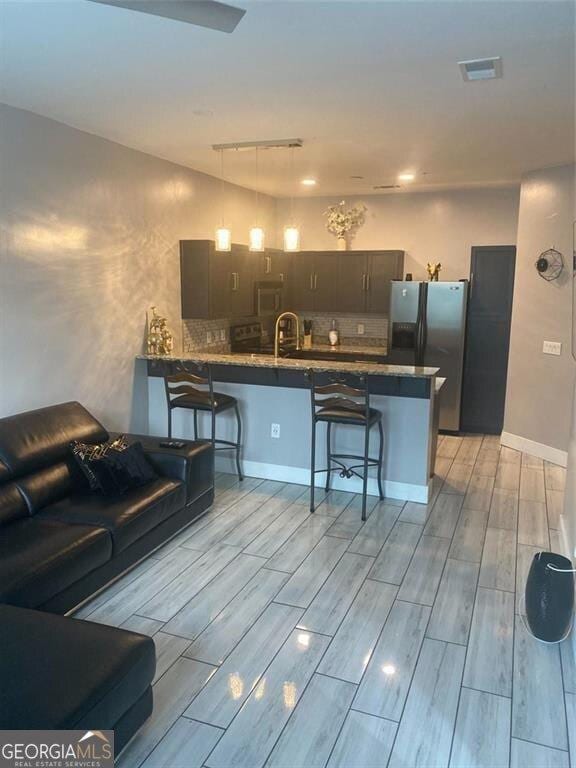 kitchen with kitchen peninsula, rail lighting, a breakfast bar, dark brown cabinets, and stainless steel fridge with ice dispenser