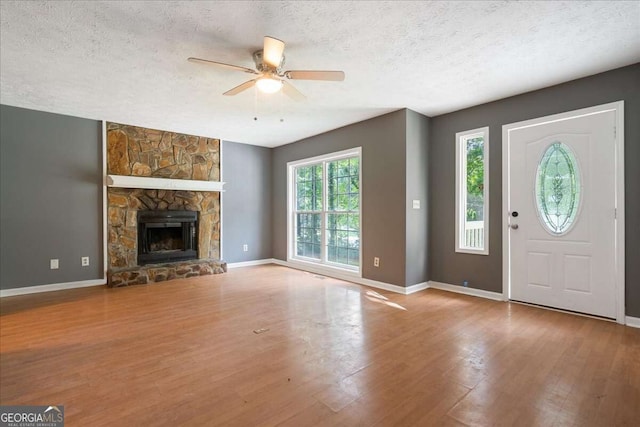 unfurnished living room featuring a textured ceiling, ceiling fan, a fireplace, and light hardwood / wood-style flooring