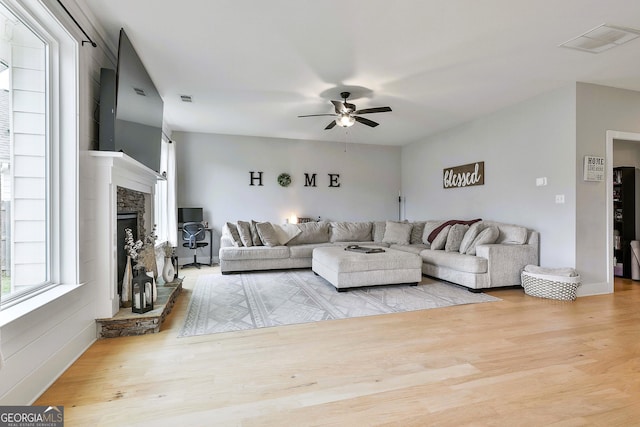 living room with ceiling fan, a stone fireplace, and light wood-type flooring