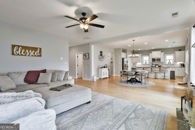 living room with ceiling fan with notable chandelier and light hardwood / wood-style floors