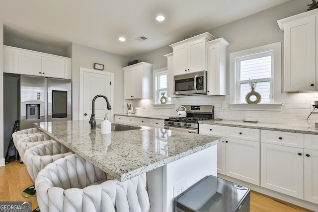 kitchen with sink, a kitchen island, a kitchen breakfast bar, white cabinets, and appliances with stainless steel finishes