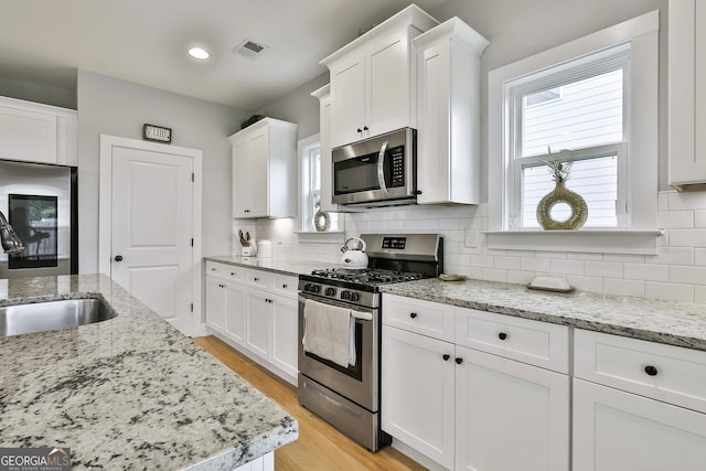 kitchen featuring appliances with stainless steel finishes, light stone counters, sink, light hardwood / wood-style floors, and white cabinetry