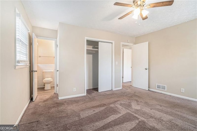 unfurnished bedroom with ceiling fan, ensuite bathroom, a textured ceiling, a closet, and carpet