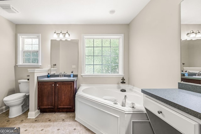 bathroom featuring vanity, a tub to relax in, toilet, and plenty of natural light