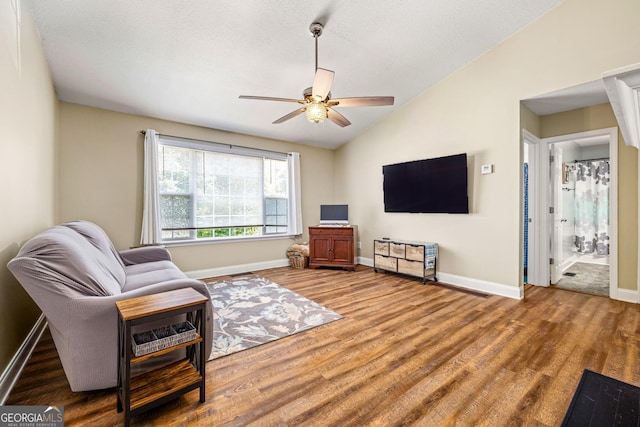 living area with ceiling fan, hardwood / wood-style floors, and vaulted ceiling