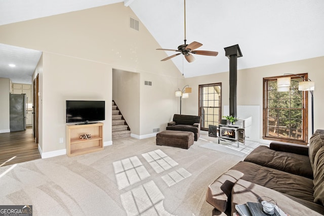 carpeted living room with high vaulted ceiling, a wood stove, and ceiling fan