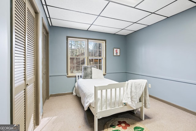 bedroom featuring light colored carpet, a paneled ceiling, and two closets