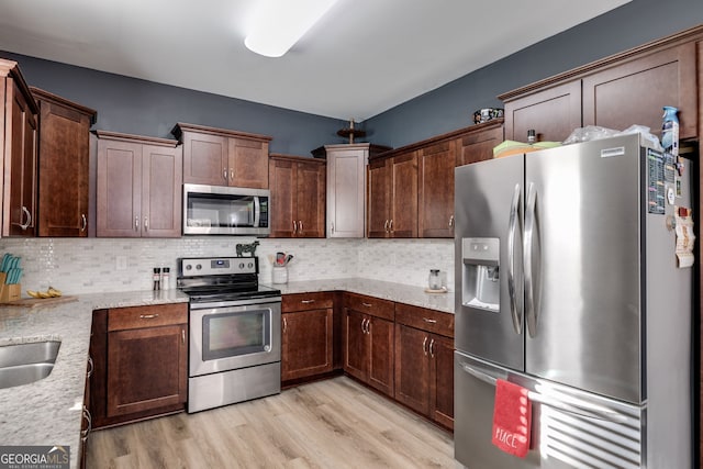 kitchen featuring light stone countertops, backsplash, stainless steel appliances, and light hardwood / wood-style floors