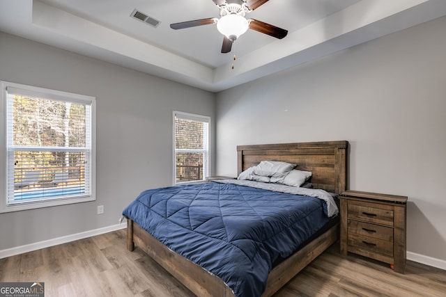 bedroom with a raised ceiling, multiple windows, ceiling fan, and hardwood / wood-style flooring