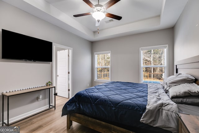 bedroom with light wood-type flooring, a tray ceiling, and ceiling fan