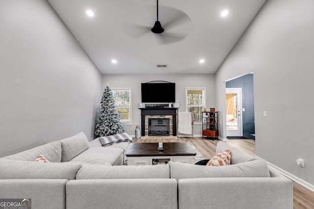 living room with a stone fireplace, ceiling fan, light hardwood / wood-style flooring, and vaulted ceiling