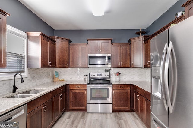 kitchen with backsplash, light stone counters, sink, and appliances with stainless steel finishes