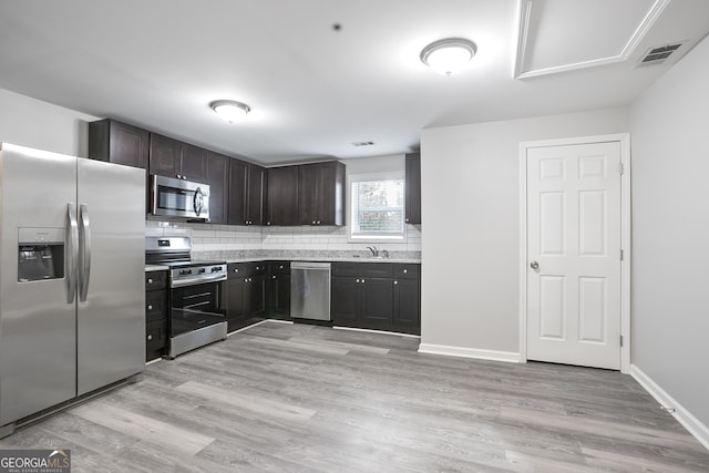 kitchen with light stone countertops, decorative backsplash, dark brown cabinets, appliances with stainless steel finishes, and light wood-type flooring