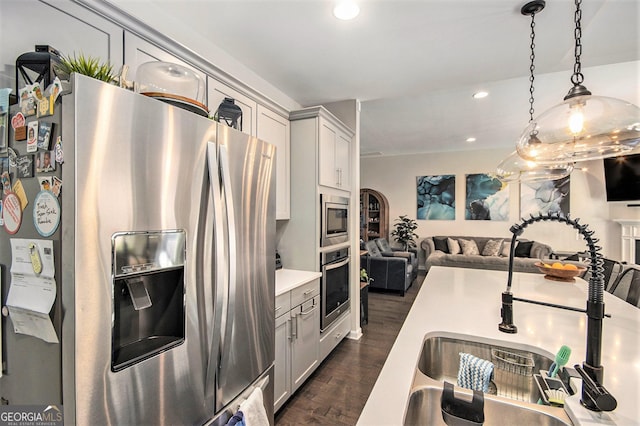 kitchen with appliances with stainless steel finishes, hanging light fixtures, dark wood-type flooring, and sink