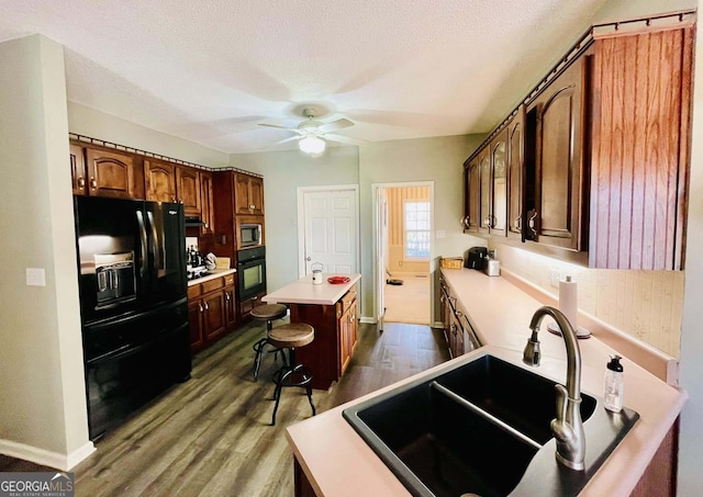 kitchen with sink, a center island, dark hardwood / wood-style floors, a kitchen breakfast bar, and black appliances