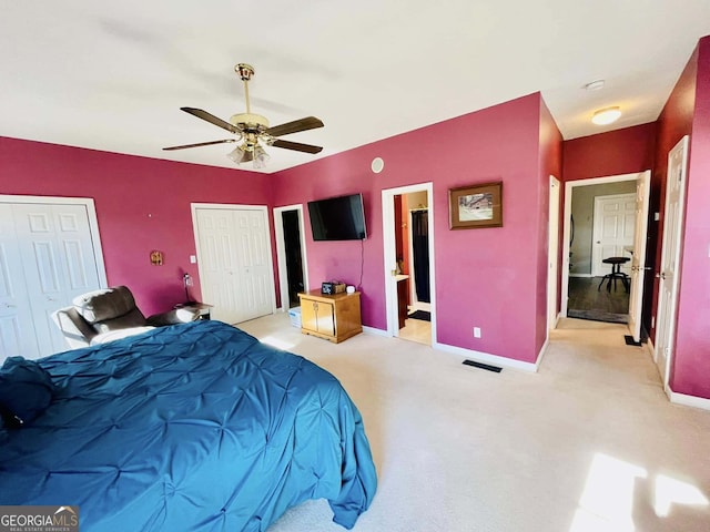 bedroom featuring ceiling fan, light colored carpet, ensuite bathroom, and two closets