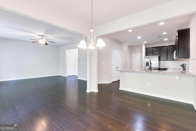 kitchen with light stone countertops, dark wood-type flooring, hanging light fixtures, stainless steel refrigerator with ice dispenser, and backsplash