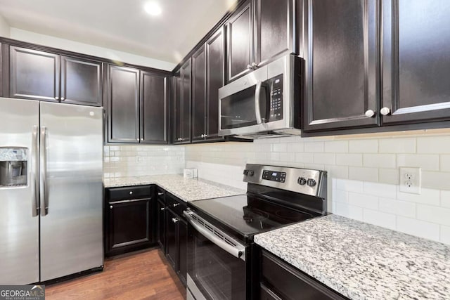 kitchen featuring dark hardwood / wood-style floors, tasteful backsplash, light stone counters, dark brown cabinetry, and stainless steel appliances