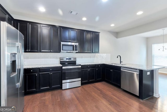 kitchen with sink, light stone counters, dark hardwood / wood-style flooring, kitchen peninsula, and appliances with stainless steel finishes