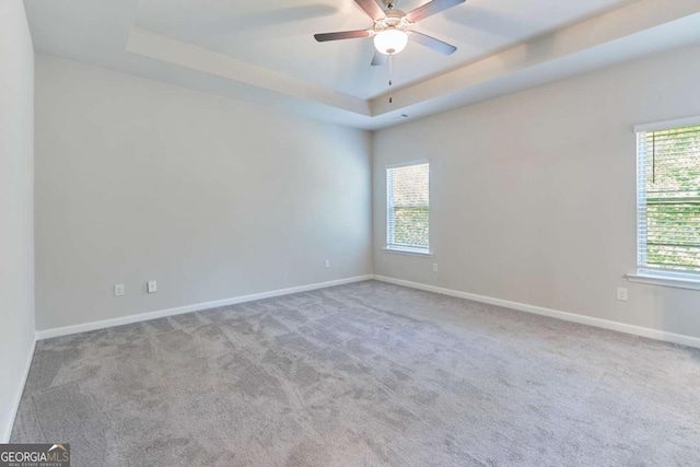 carpeted empty room with ceiling fan, a healthy amount of sunlight, and a raised ceiling