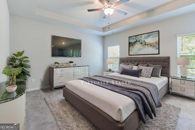 bedroom with multiple windows, a tray ceiling, and ceiling fan