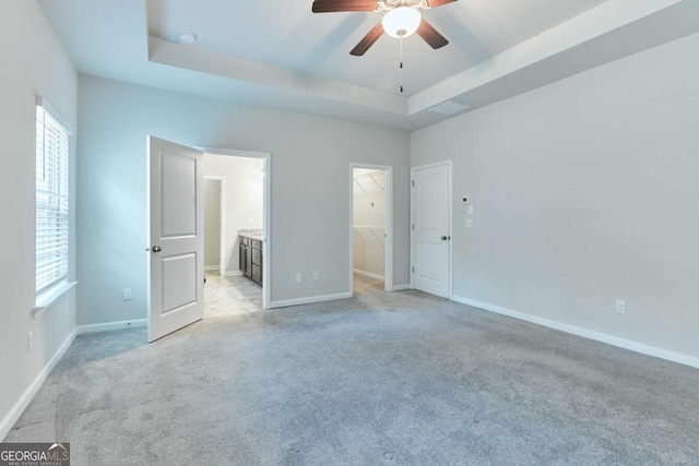 unfurnished bedroom with light carpet, a raised ceiling, ceiling fan, a spacious closet, and a closet