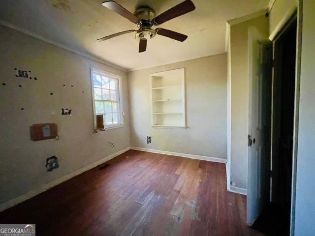 empty room with crown molding, ceiling fan, dark hardwood / wood-style flooring, and built in shelves